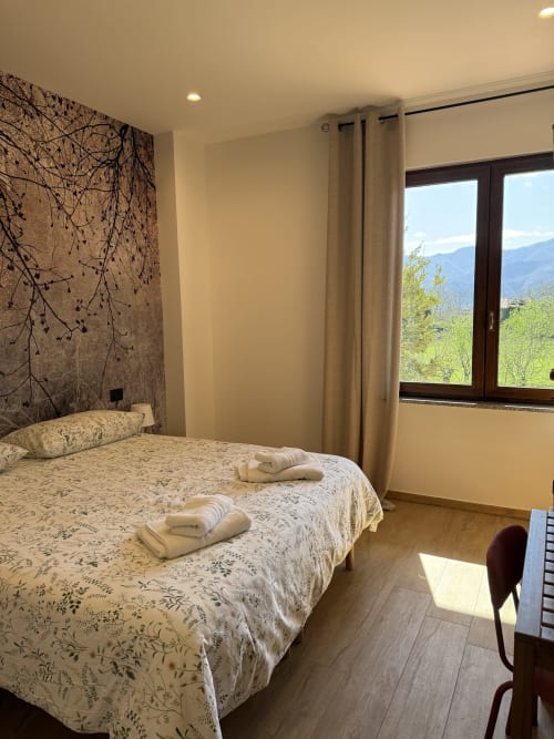 Camera luminosa del B&B Luna Verde con letto matrimoniale, vista sulle montagne dalle ampie finestre e arredi moderni in Italia.