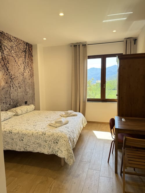 Luminosa camera matrimoniale con vista montagna presso Luna Verde B&B, con testata decorativa, biancheria color crema e mobili in legno