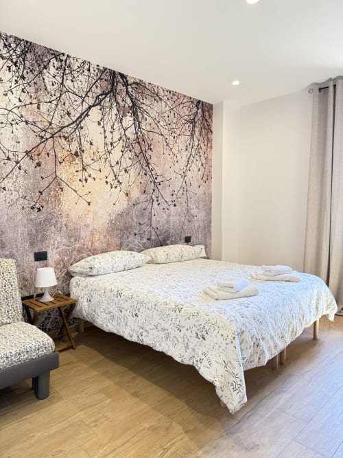 Camera da letto moderna con letto matrimoniale, murale botanico, biancheria bianca, pavimenti in legno e vista giardino presso B&B Luna Verde