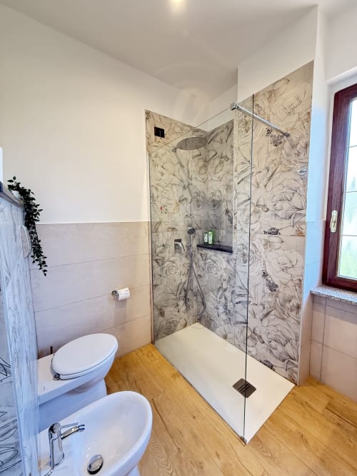 Bagno moderno con doccia walk-in, piastrelle decorate, sanitari bianchi e pavimento in legno presso B&B Luna Verde