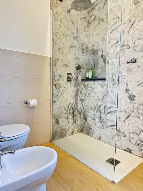 Moderno bagno del B&B Luna Verde con doccia aperta, piastrelle floreali, sanitari bianchi, pavimentazione in legno e carta igienica