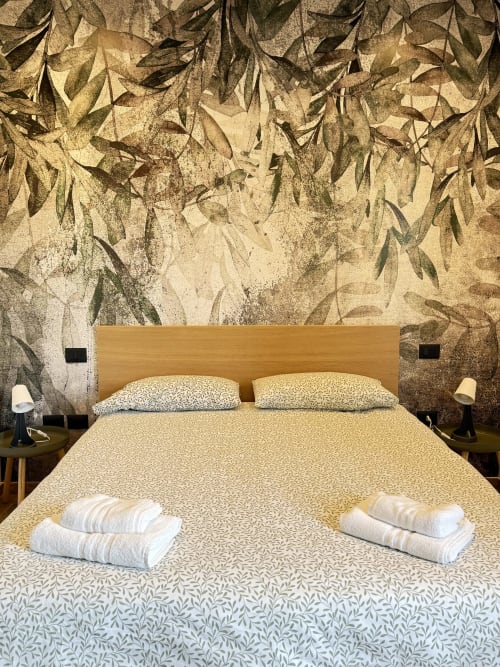 Camera moderna presso B&B Luna Verde con letto in legno, asciugamani bianchi, carta da parati botanica con motivi fogliari e vista sul giardino