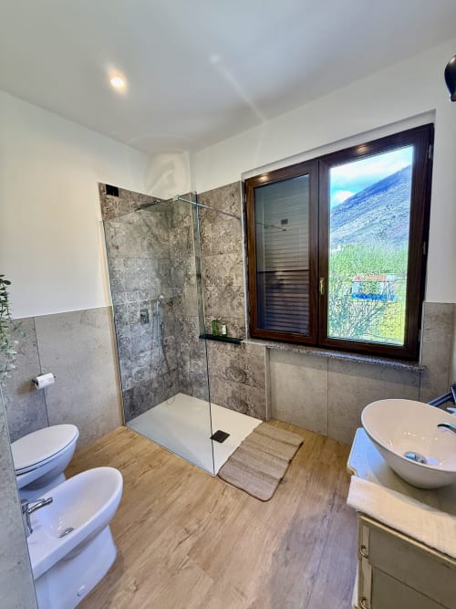 Bagno moderno della B&B Luna Verde con doccia a filo pavimento, toilet, bidet, lavabo, pavimento in legno e vista sulle montagne