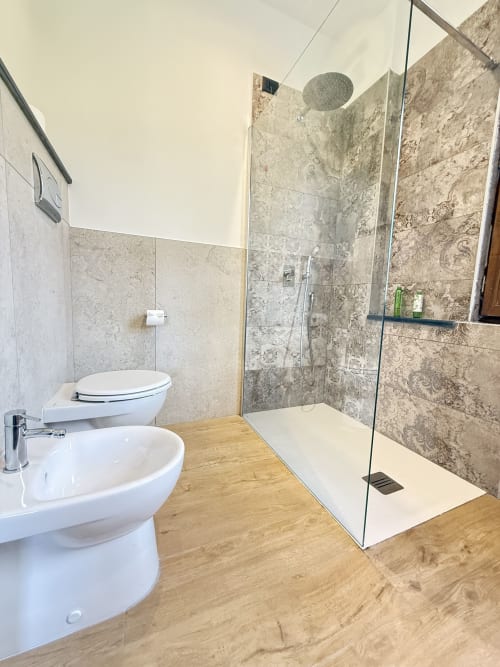 Bagno moderno con toilette bianca, bidet, doccia walk-in con box in vetro e soffione a cascata presso B&B Luna Verde