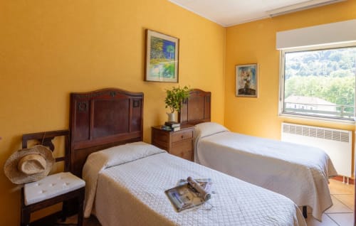 Camera da letto giallo brillante con due letti singoli, testate in legno, vista sul lago e arredamento rustico al Lake Orta Retreat