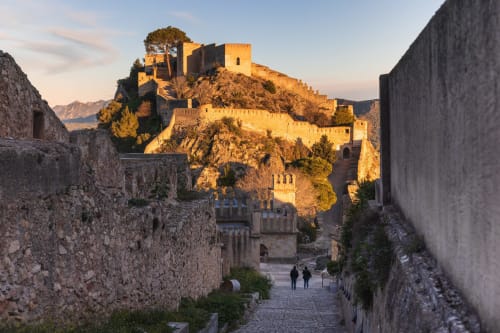 Historic castle fortress overlooking Rafelguaraf, Spain at sunset with stone pathways and mountains in background