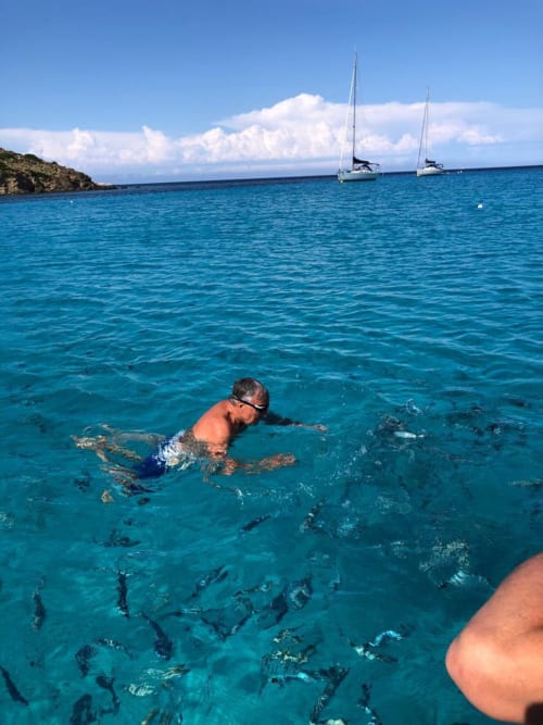 Giovane nuotatore che fa snorkeling in acque turchesi vicino a barche a vela presso Pescaturismo Lia, Stintino
