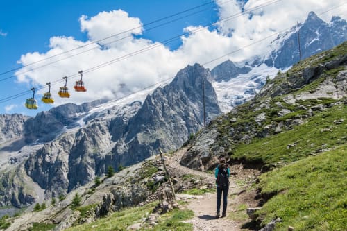 Randonneur sur sentier montagnard avec téléphérique et pics enneigés près de l'hôtel Le Monêtier-les-Bains