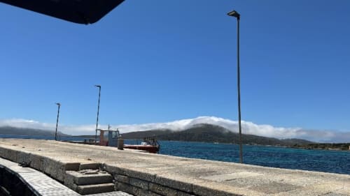 Barca da pesca ormeggiata al porto di Stintino con montagne e mare blu, Pescaturismo Lia