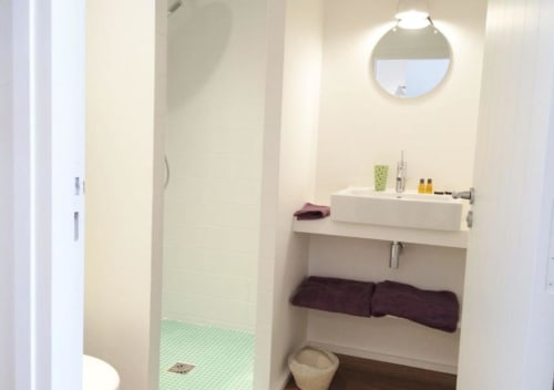 Salle de bains moderne du studio Denis & Virginie à Versailles, avec lavabo blanc, miroir rond et carrelage vert
