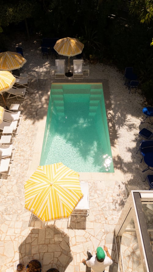 Aerial view of Hotel Le Sud's pool in Juan Les Pins with yellow umbrellas, loungers, and surrounding lush greenery