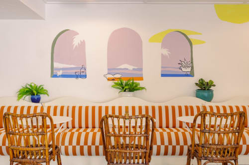 Salon de l'Hôtel Le Sud avec sièges à rayures orange, chaises en rotin, plantes en pot et fresques murales aux motifs côtiers à Juan les