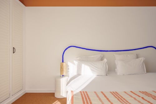 Chambre moderne de l'Hôtel Le Sud avec tête de lit bleue, literie blanche et plafond accentué d'orange à Juan-les-Pins