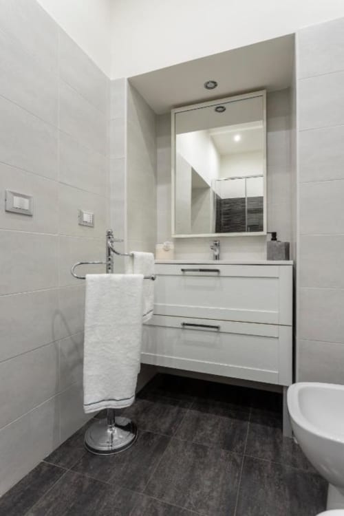 Modern bathroom in Exclusive Domus Gaudia Junior Suite with white vanity, large mirror, dark tile flooring, and guest
