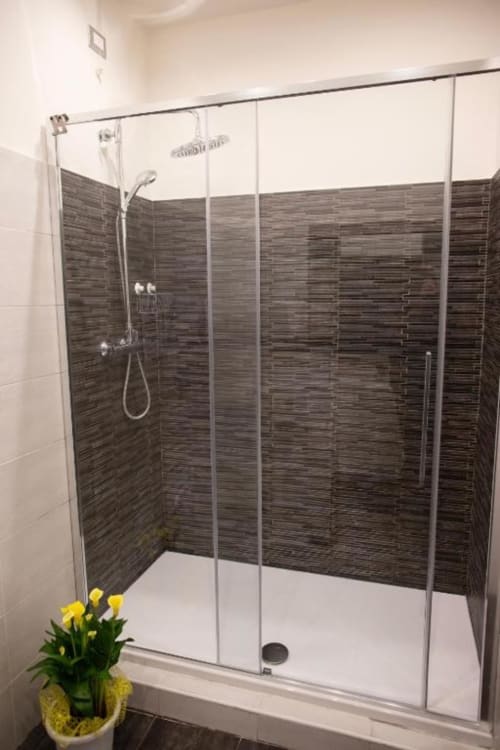 Modern walk-in shower with dark stone tile walls and glass enclosure at Exclusive Domus Gaudia hotel in Rome, yellow flowers