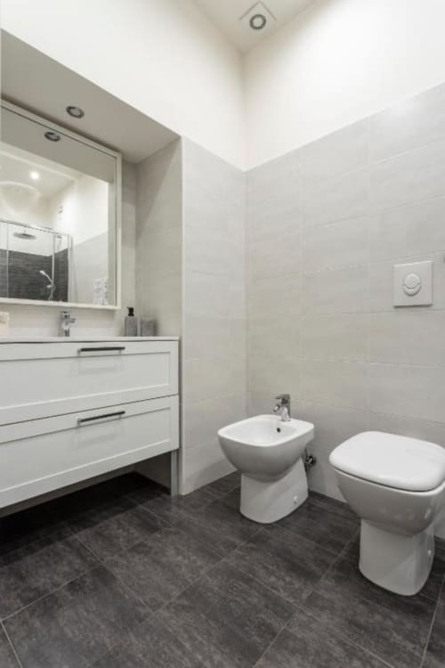 Modern bathroom in Exclusive Domus Gaudia Junior Suite Rome, featuring white vanity, bidet, toilet, and dark tile flooring