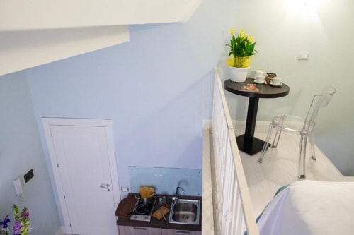 Junior Suite kitchenette at Exclusive Domus Gaudia Roma with sink, stovetop, yellow flowers on side table, and clear chairs