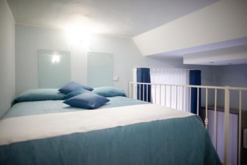 Modern Junior Suite bedroom at Exclusive Domus Gaudia Roma with queen bed, blue pillows, glass panels, and white railings.