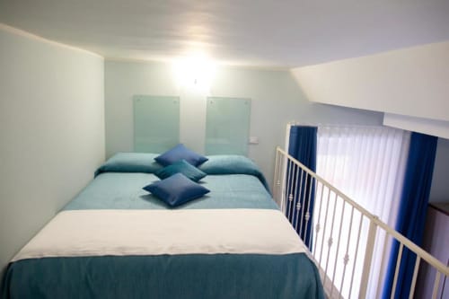 Modern bedroom in Rome's Exclusive Domus Gaudia with queen bed, blue accents, and city view from windows