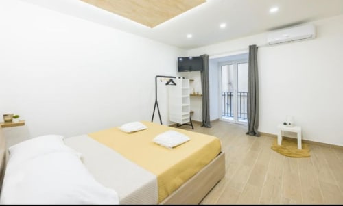 Camera moderna a Casa Fernanda a Napoli con biancheria gialla, TV, accesso al balcone, cucina e zona living completamente attrezzate