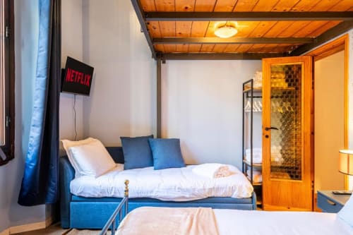 Camera moderna presso Bronze Horse Affittacamere a Firenze con letto blu, TV Netflix, soffitto in legno e porta in legno arancione