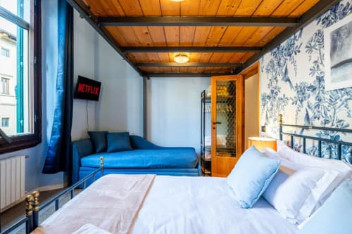 Camera moderna presso Bronze Horse Affittacamere a Firenze con divano blu, soffitto in legno e carta da parati botanica