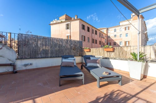 Terrazza sul tetto di Terrestre Roma con lettini, staccionata in legno, piante in vaso e storici edifici romani sotto cielo azzurro