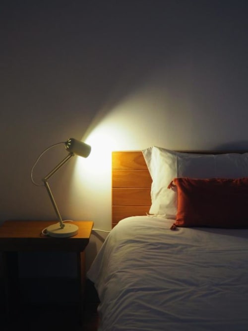 Quarto aconchegante na Quinta da Coutada com luminária de mesa acesa, cabeceira de madeira e roupa de cama branca com almofadas vermelhas