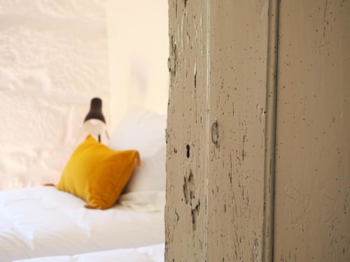 Porta rústica do quarto da Casa do Meio na Quinta da Coutada, revelando roupa de cama branca e almofada amarela em Arcos de
