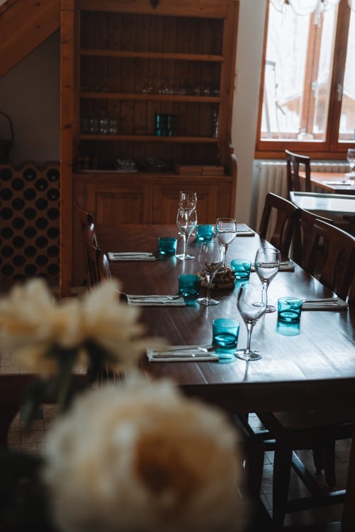 Formal dining room at Auberge du Pont de l'Alp with set table, turquoise glassware, and wooden hutch backdrop.