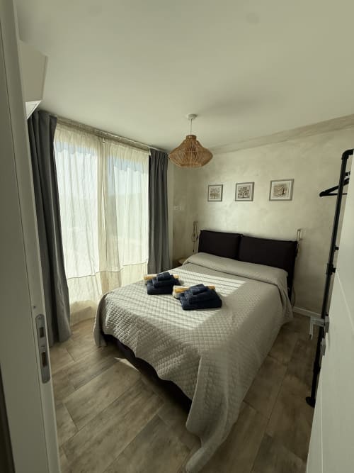 Bright bedroom with queen bed, black headboard, woven pendant light, and sea view balcony at Sardinia Holidays villa in Torpè