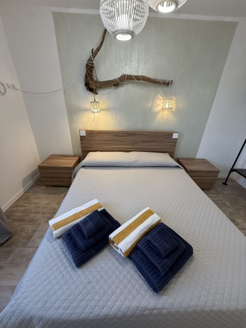 Modern bedroom at Sardinia Holidays in Torpè with wooden bed frame, folded towels, decorative driftwood, pendant lights, and