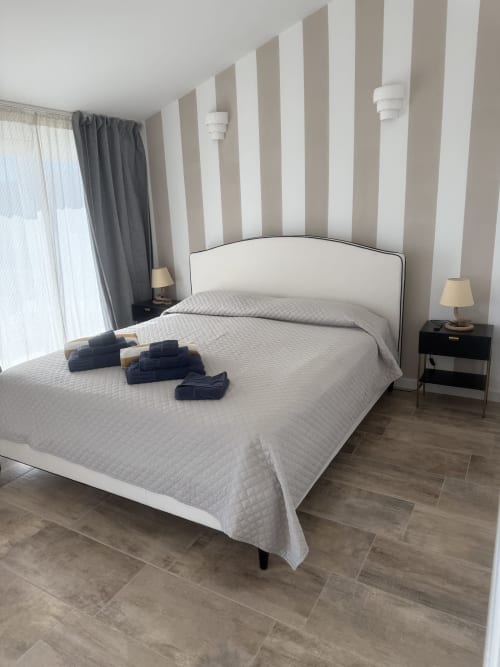 Elegante suite padronale a Sardinia Holidays con pareti righe, letto bianco, vista mare e arredi contemporanei