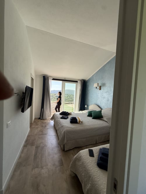 Camera deluxe spaziosa presso Sardinia Holidays con due letti, parete accent blu, balcone con vista su montagne e giardino