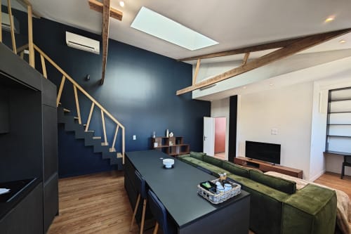 Salon loft moderne de l'hôtel O LIT avec mur bleu marine, poutres bois, canapé vert et escalier ouvert