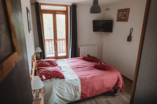 Chambre lumineuse à l'Auberge du Pont de l'Alp avec literie rose, portes de balcon, TV et vue sur les montagnes au Monêtier-les-Bains.