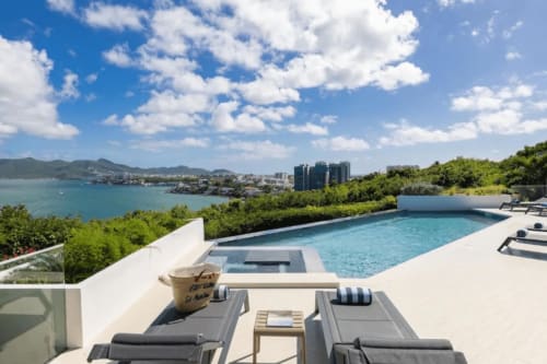Terrasse de piscine luxueuse surplombant la baie turquoise de l'hôtel O LIT avec transats, bain à remous et vue sur la skyline