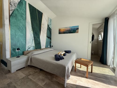 Modern bedroom at Sardinia Holidays with queen bed, turquoise accent wall, ocean view, and direct pool access in Torpè