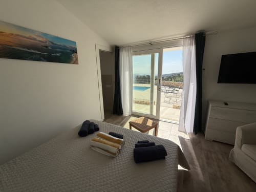 Bright bedroom with direct pool access at Sardinia Holidays, featuring sea view through glass doors and patio furniture
