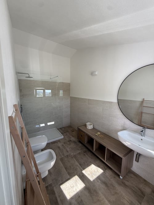 Modern bathroom at Sardinia Holidays with walk-in shower, dual sinks, heated towel rack, and tiled flooring