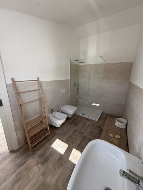 Modern bathroom in Sardinia Holidays with bidet, toilet, walk-in shower, wooden towel rack, and dark wood-look flooring