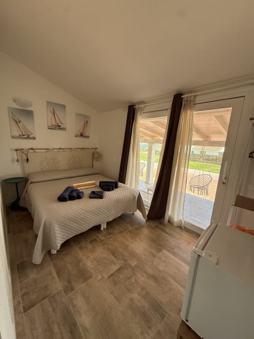 Bright bedroom at Sardinia Holidays with queen bed, ocean view through glass doors opening to private veranda in Torpè