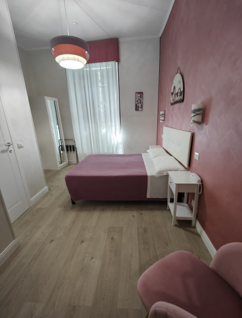 Camera moderna dell'Hotel Principe Amedeo con biancheria bordeaux, testata bianca, lampada a sospensione e pareti rosa