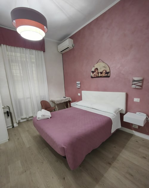 Camera Matrimoniale Economy Hotel Principe Amedeo con pareti color malva, testata bianca, illuminazione moderna, aria condizionata e vista sulla città