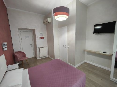 Camera moderna dell'Hotel Principe Amedeo con letto viola, TV a schermo piatto, lampada a sospensione e arredi contemporanei