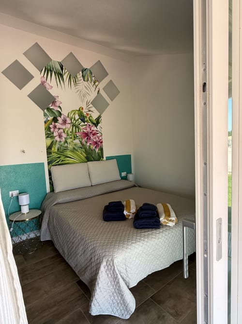 Tropical Room queen bed with floral artwork, teal headboard, ocean view at Sardinia Holidays Torpè