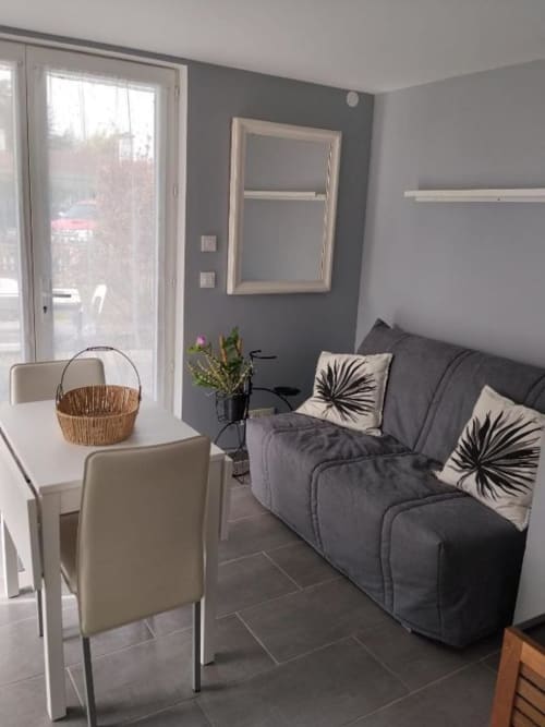 Modern living room at La Pause Landaise with gray sofa, white shelving, garden view, and dining area in Magescq