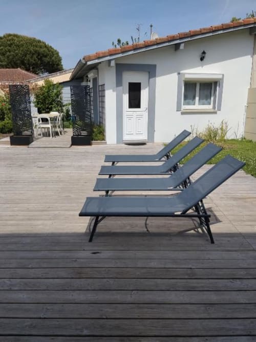 Three dark lounge chairs on wooden deck outside modern white cottage at La Pause Landaise in Magescq
