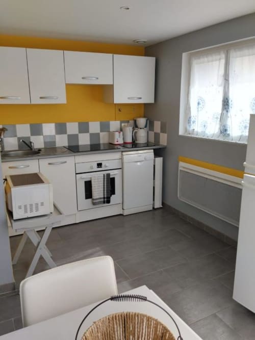 Modern kitchen with white cabinets, yellow accents, checkered backsplash, and dining area in Le Petit Baigneur at La Pause
