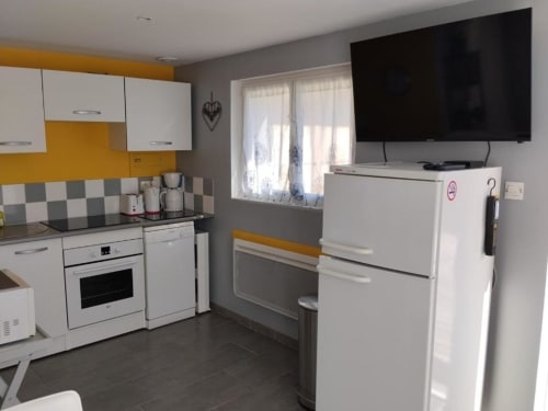 Modern kitchen in Le Petit Baigneur room at La Pause Landaise, Magescq, with white appliances, yellow accents, and TV.